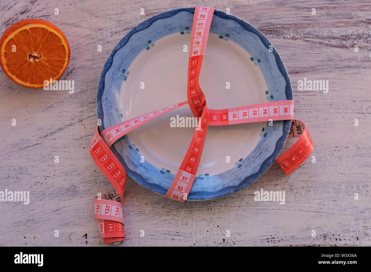 Eine halbe orange Frucht auf Teller mit Maßband, Messer und Gabel. Ernährung Lebensmittel auf hölzernen Tisch. Gewichtskontrolle - Bild Stockfoto