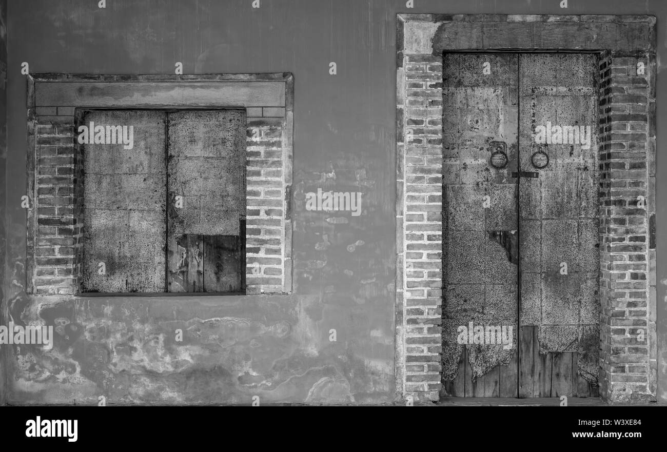 Alte weiße und graue Mauer des alten Gebäudes. Beton- und Ziegelgebäude mit geschlossener Tür und Fenster. Die Außenseite des alten Gebäudes. Zement Stockfoto