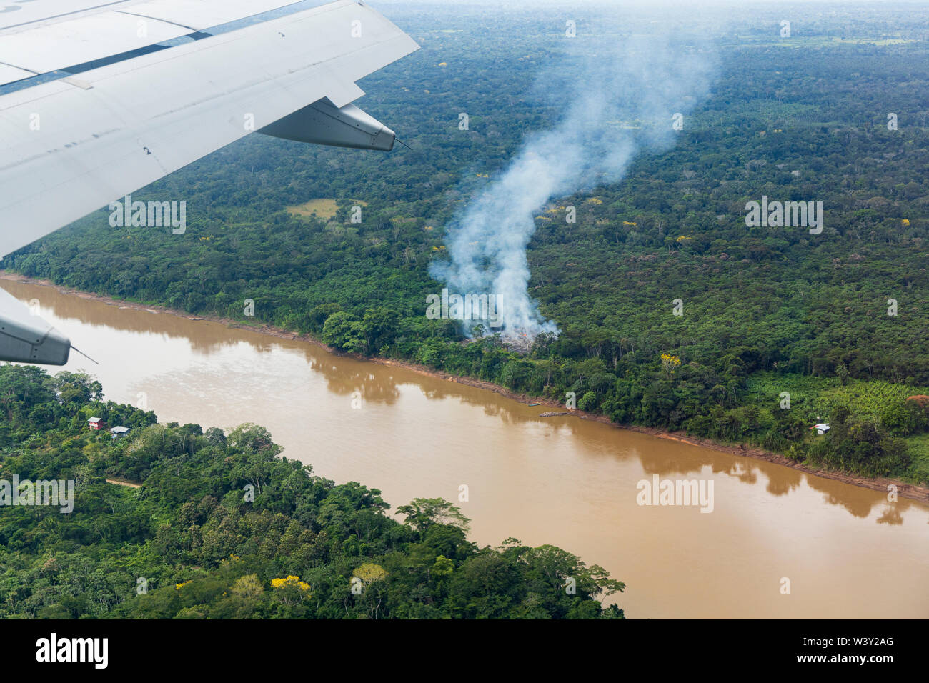 Luftaufnahme von innen ein Passagierflugzeug über dem Fluss und Rauch von einem Feuer Clearing für Brandrodung Landwirtschaft in Amazonien von Peru, Südafrika Stockfoto