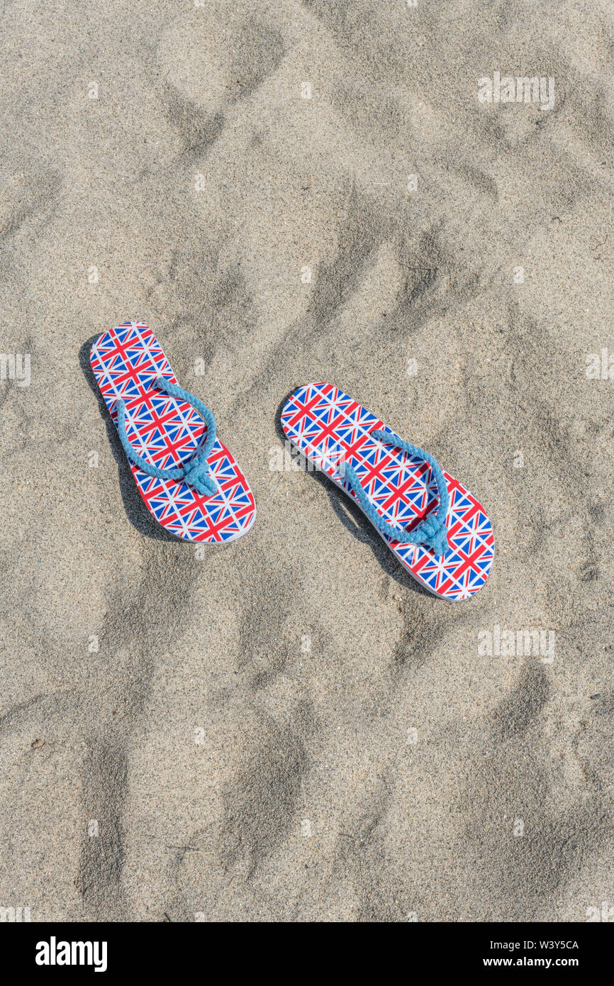 Flipflops mit GB-Flagge / Union Jack am Sandstrand - für 2021 Aufenthalte in Großbritannien, Urlaub zu Hause, Aufenthalt in Cornwall, Badeurlaub, Flip-Flop-Schuhe. Stockfoto