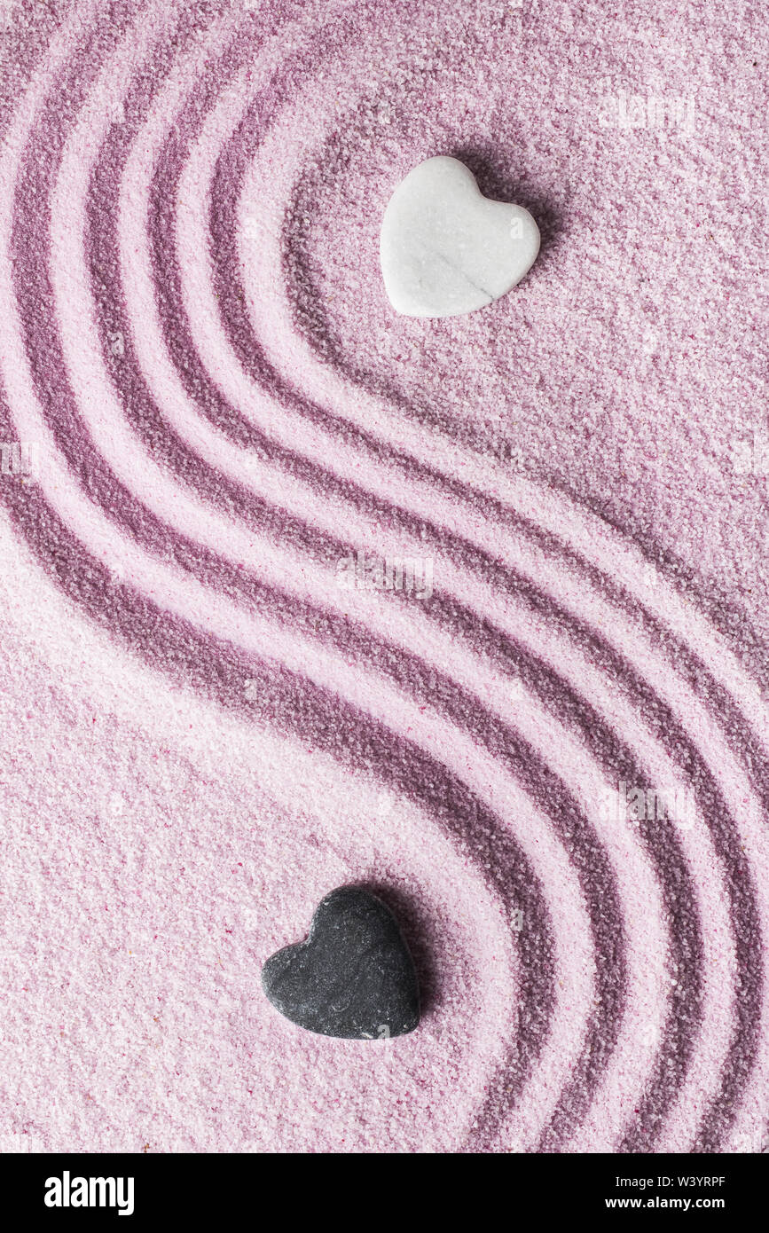 Zwei steinerne geformte Herzen weiß, der andere schwarz auf rosa Sand Stockfoto