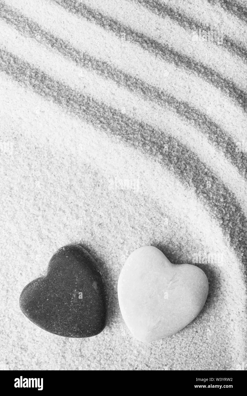Zwei steinerne geformte Herzen weiß, der andere schwarz auf rosa Sand Stockfoto