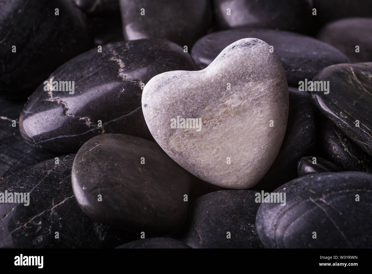 Hintergrund mit schwarzen Steinen und über einen weißen Stein Herz Stockfoto