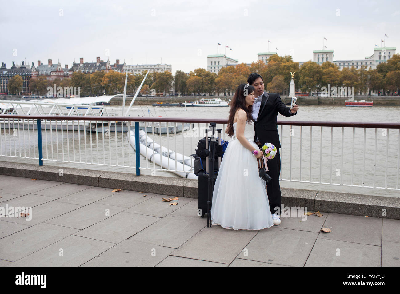 Paar posieren für selfie in Hochzeit Kleidung mit London Kulisse der Themse, South Bank und des Parlaments Stockfoto