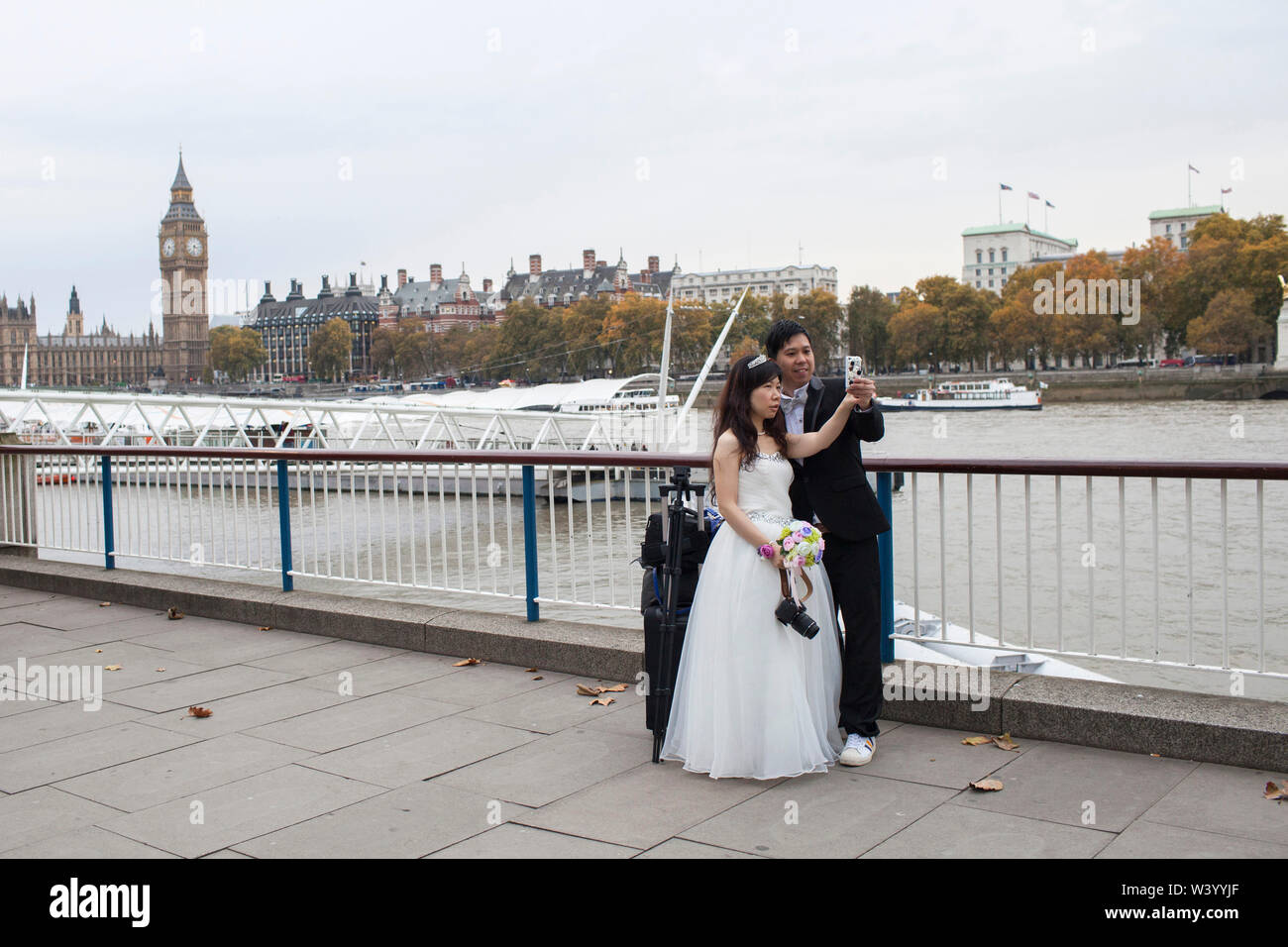 Paar posieren für selfie in Hochzeit Kleidung mit London Kulisse der Themse, South Bank und des Parlaments Stockfoto