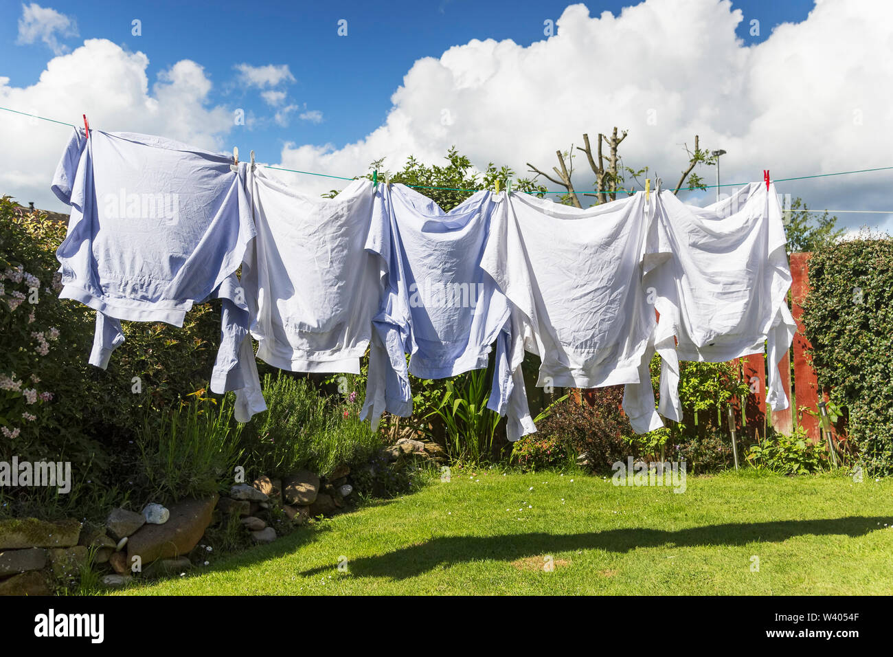 Shirts trocknen auf die Wäscheleine in Großbritannien Garten mit blauen Himmel und weiße, flauschige Wolke. Stockfoto