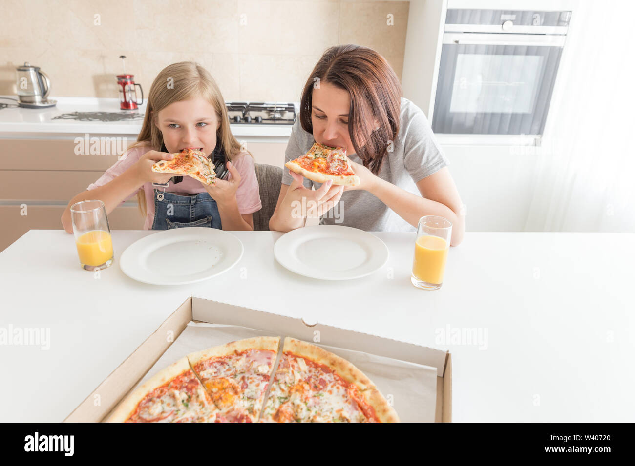 Mutter und Tochter in der Küche sitzen, essen Pizza und Spaß haben. Fokus auf Tochter Stockfoto