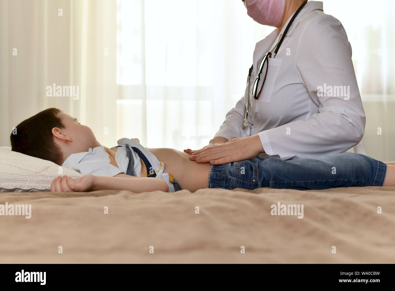 Der Arzt sitzt am Bett des kranken Kindes und untersucht den Bauch. Der Junge drehte den Kopf zur Seite und ruhig ihre Handlungen beobachtet. Stockfoto