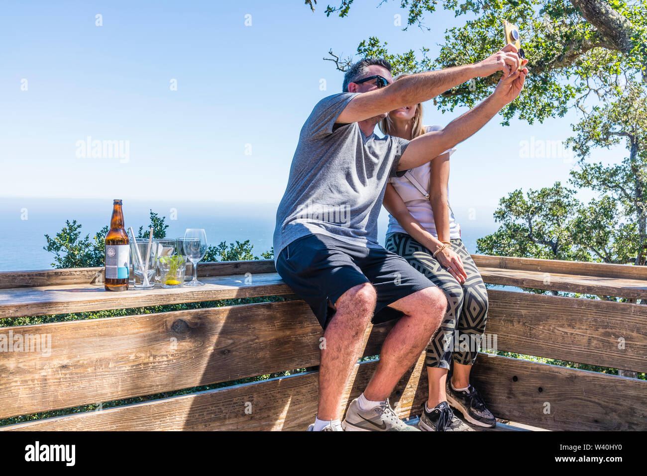 Einem erwachsenen Paar sitzt auf einer Holzbank mit Blick auf die Central Coast Kalifornien und nimmt eine selfie ihre Reise zu dokumentieren. Stockfoto