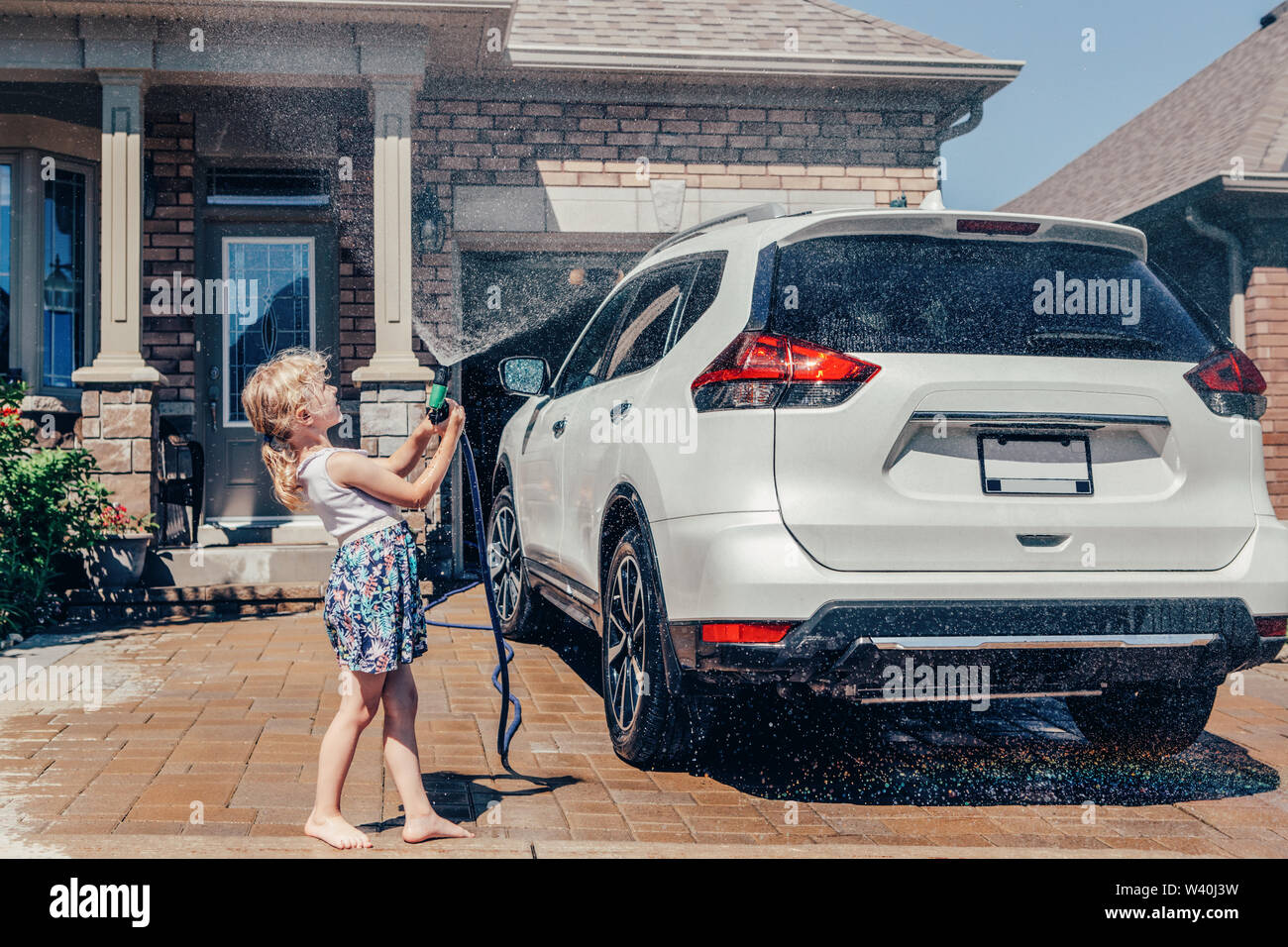 Vorschule wenig Kaukasische Mädchen waschen Auto in der Einfahrt vor dem Haus auf sonnigen Sommertag niedlich. Kids home Besorgungen Pflicht aufgaben verantwortung Konzept. Stockfoto