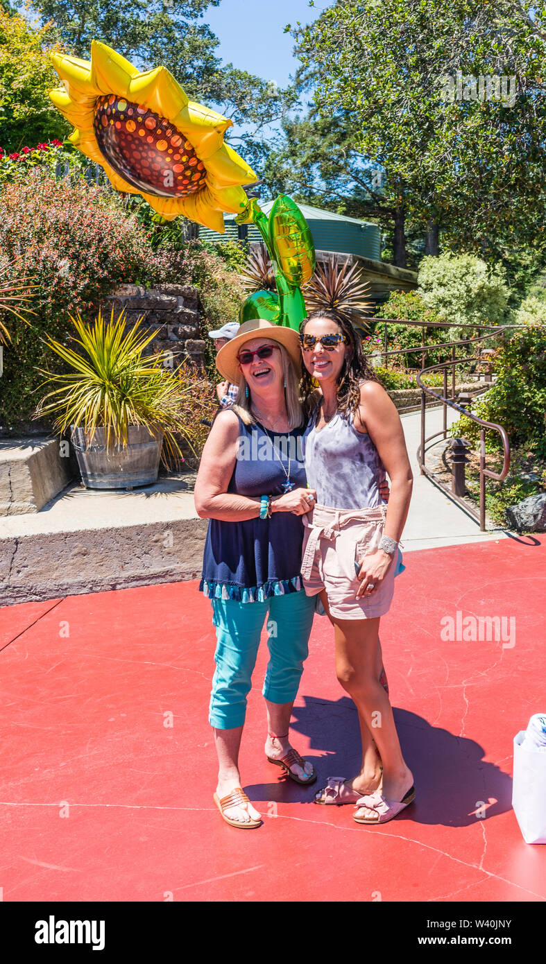 Zwei weibliche Millennials feiern ihre Geburtstage mit einem riesigen Sonne geformten Mylar Ballon auf der Terrasse des Nepenthe Restaurant auf dem Highway 1. Stockfoto