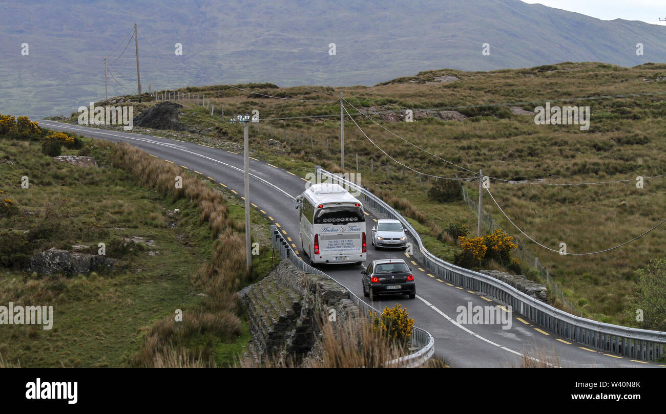 Ein Reisebus und Pkw auf einem schmalen hügeligen Land Straße in der Grafschaft Galway, Irland mit einem Auto, das hinter dem Trainer. Stockfoto