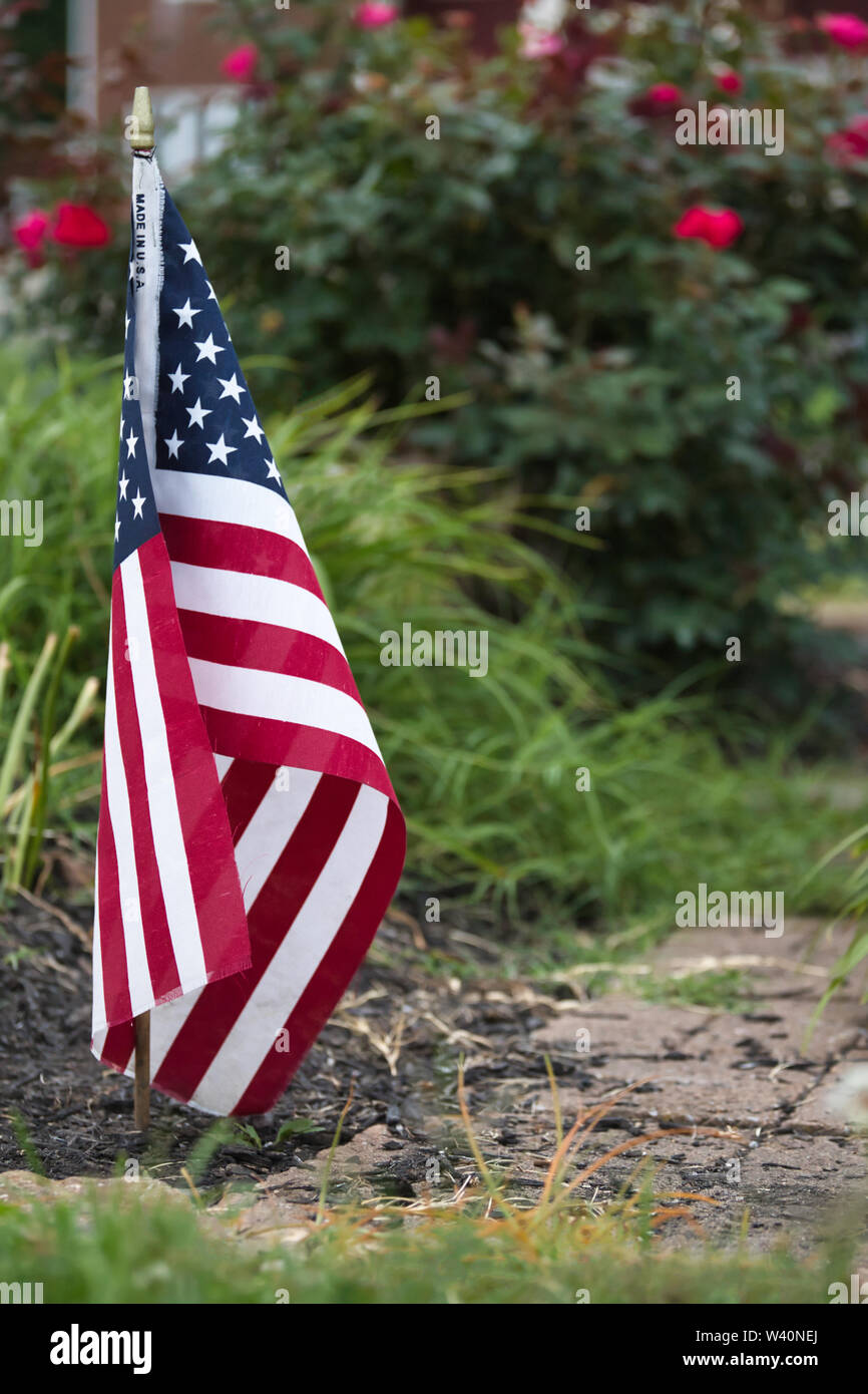 Kleine Flagge in einem Garten mit Ziegel Gehweg vor einem Rosenbusch. 'Make' ist in den USA auf die Fahne geschrieben. Stockfoto