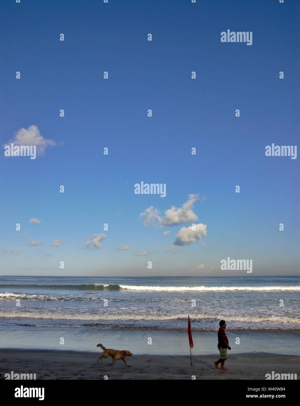 Strand von Kuta, Bali, Indonesien - Juni 2019: Menschen laufen mit Hund am Strand mit einer Flagge. Stockfoto