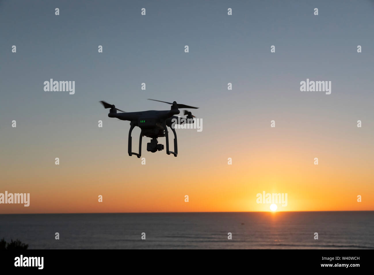 Professionelle Drohne fliegen bei Sonnenaufgang über dem Meer. Der Himmel glüht Stockfoto