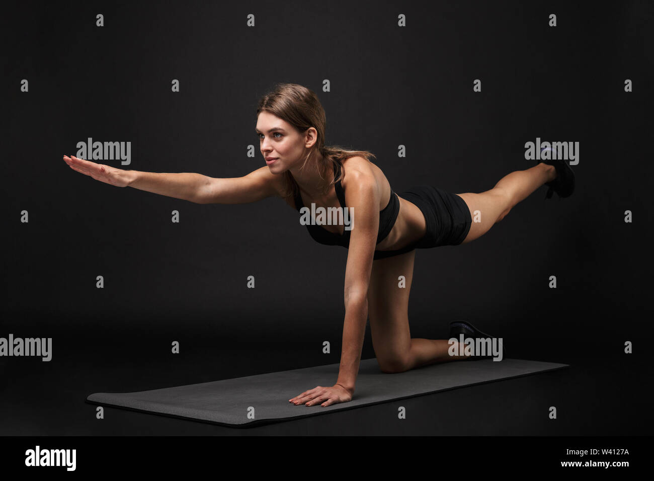 Attraktive selbstbewussten jungen Frau tragen gesunde Fitness Sport-BH und Shorts über schwarzen Hintergrund isoliert, Ausübung auf einem Fitness Matte, Yoga stret Stockfoto