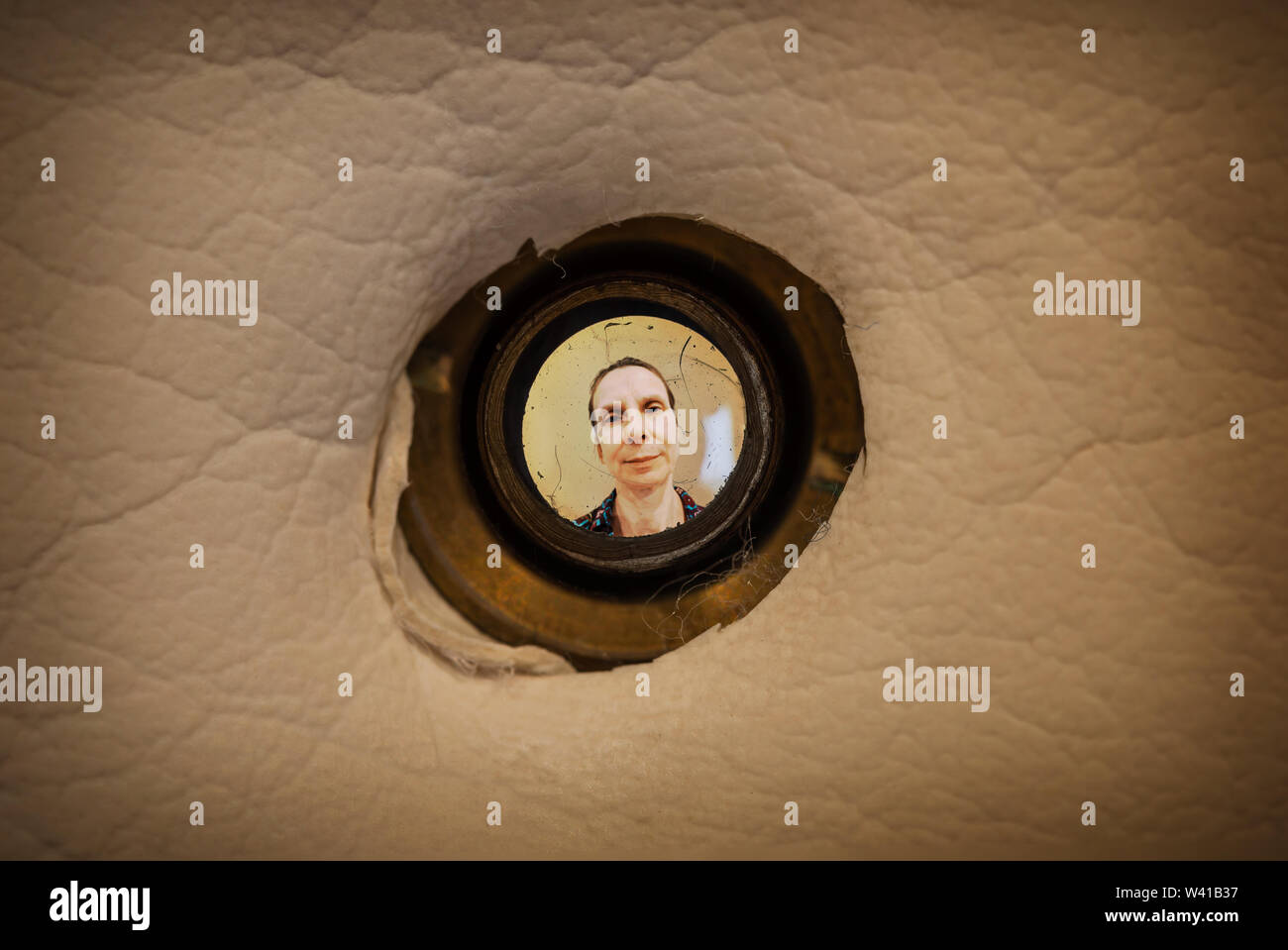 Frau unscharf durch das alte schmutzige Guckloch der vorderen Tür in einer dunklen Wohnung gesehen Stockfoto