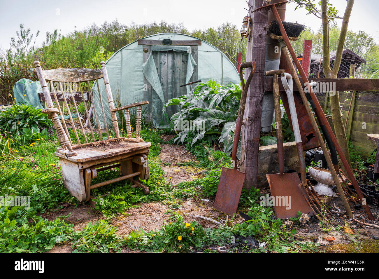Garten mit Gewächshaus, alt und rostet Garten Werkzeuge und Ausrüstung und einem alten hölzernen Schaukelstuhl, Kilwinning, Ayrshire, Schottland, Großbritannien verlassen Stockfoto