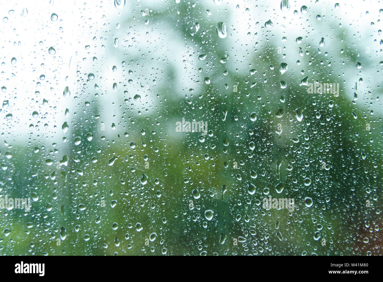 Regen fällt auf regnerischen Tag auf außen Fenster Glas mit unscharfen Rändern. Regen vor Fenster im Frühling. Wassertropfen Fließen der Oberfläche. Stockfoto