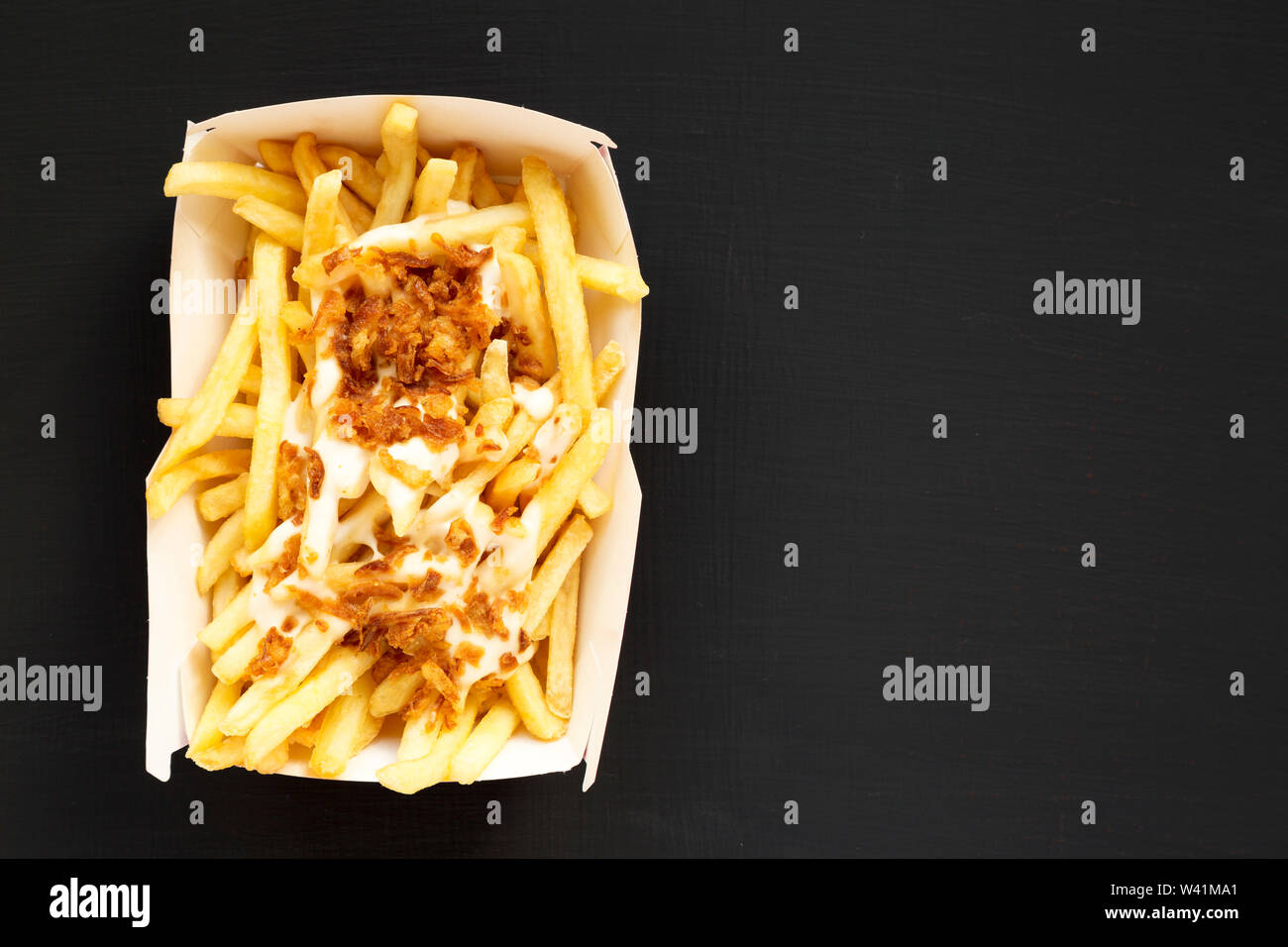 Pommes Frites mit Käsesoße und Zwiebel in einem Papier, das auf einer ...