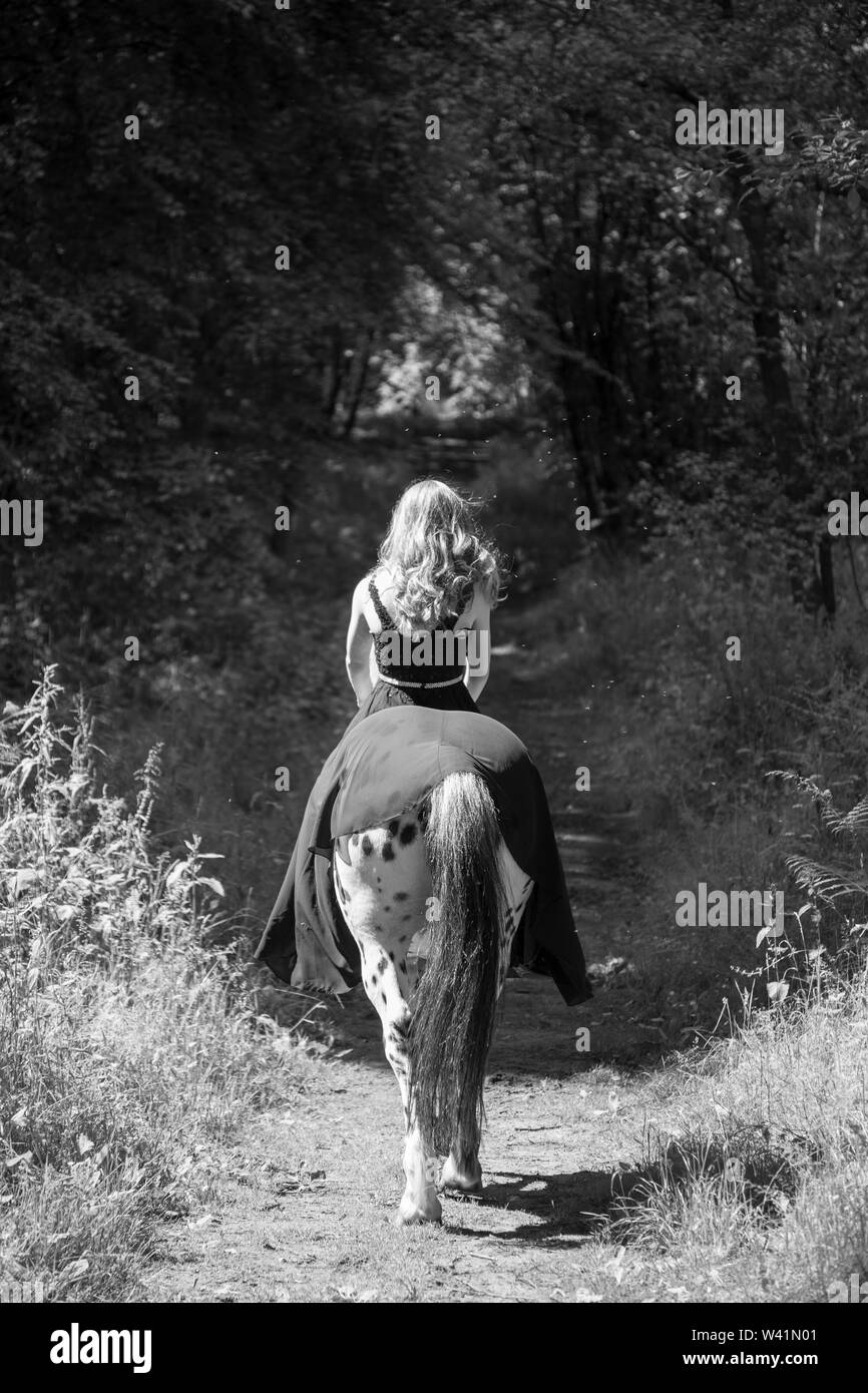 Junge Mädchen reiten ihr Pferd in einem Langen fließenden kleid, in der grünen Wälder in Shropshire Landschaft, von der Kamera entfernt sein, damit wir ihr Gesicht nicht sehen kann Stockfoto
