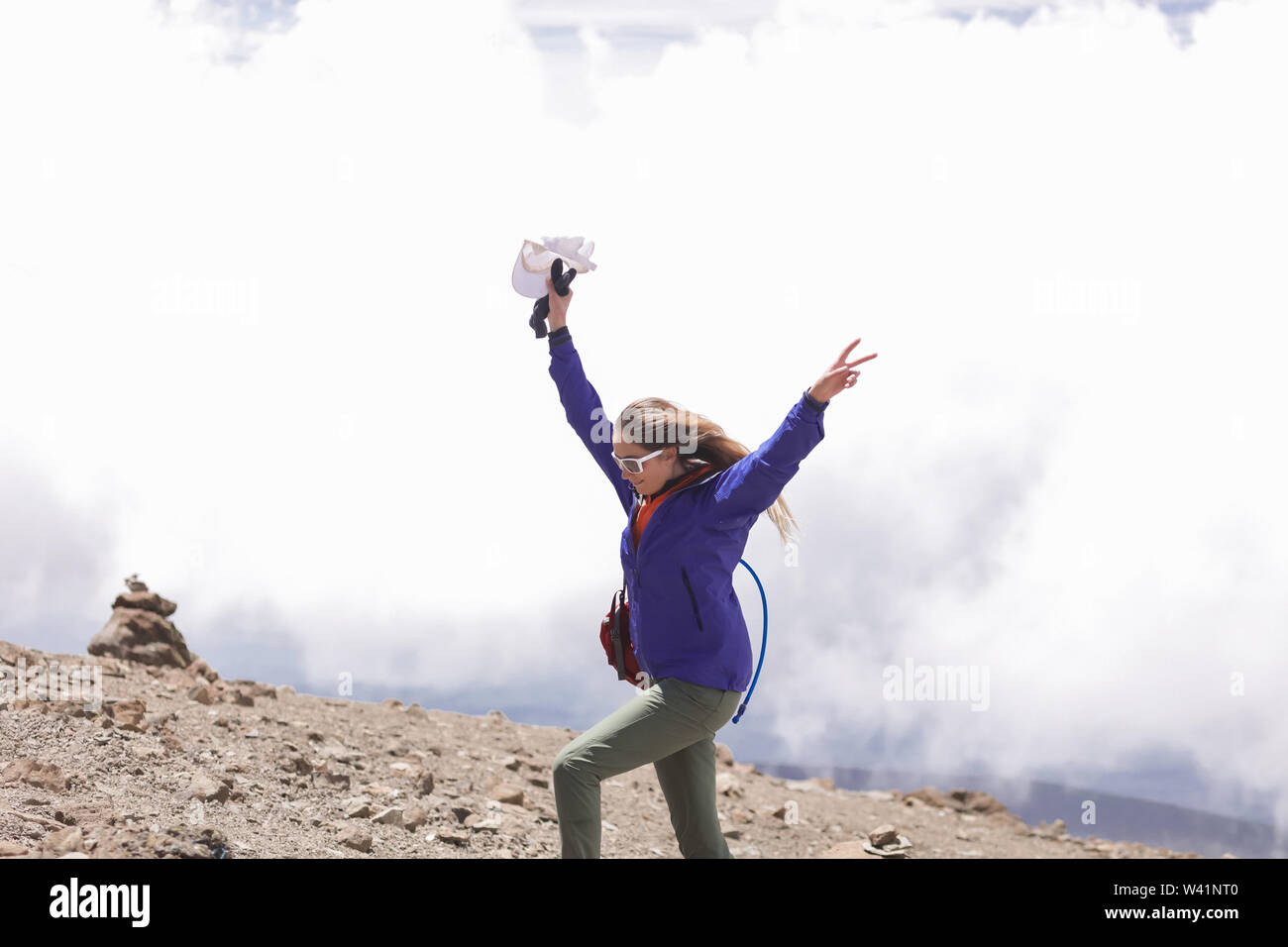 Hübsche Frau genießt ihre extreme Reise auf den Afrikanischen Berge. Tragen Moderne blaue Jacke, Grau Hose und sunglasees. Lange blonde Haare wehenden Wind Stockfoto