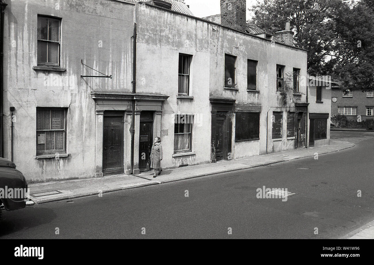 Anfang der 1970er Jahre, historische, eine Dame zu Fuß entlang einer schmalen Bürgersteig neben einer alten viktorianischen Terrasse Gehäuse, einige verlassen, im Charlton Village, South London, England, Stockfoto