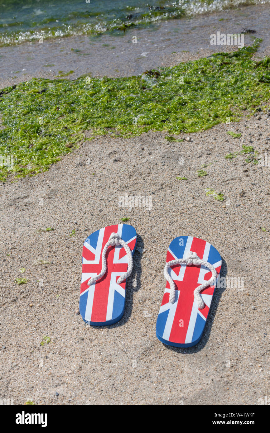 Flipflops mit GB-Flagge / Union Jack am Sandstrand - für 2021 Aufenthalte in Großbritannien, Urlaub zu Hause, Aufenthalt in Cornwall, Badeurlaub, Flip-Flop-Schuhe. Stockfoto