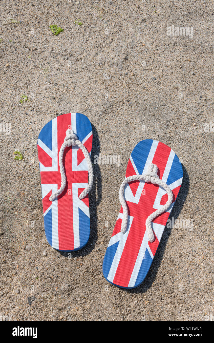 Flipflops mit GB-Flagge / Union Jack am Sandstrand - für 2021 Aufenthalte in Großbritannien, Urlaub zu Hause, Aufenthalt in Cornwall, Badeurlaub, Flip-Flop-Schuhe. Stockfoto