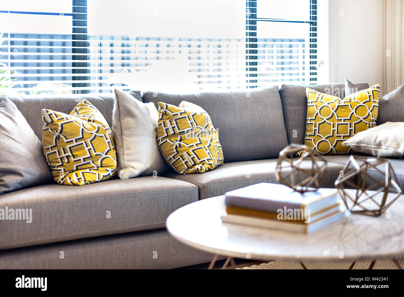 Gelb und Grau Farbe Kissen auf dem Sofa neben einem Fenster, die das Tageslicht in die Zimmer mit unscharfen Bücher und phantastischen acht Fasen Spreads Stockfoto