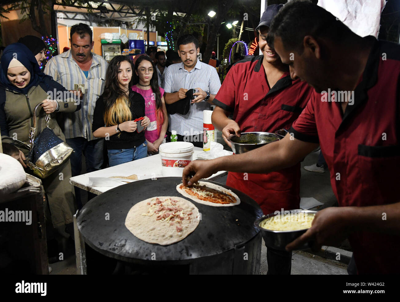 Damaskus, Syrien. 18 Juli, 2019. Syrer warten Essen während einer Unterhaltung Festival genannten Ham (Damaskus) Sammelt Uns' in Damaskus, Syrien, 18. Juli 2019. Das Festival inklusive Folkloredarbietungen, Kinder Spiele und Verkostungen. Credit: Ammar Safarjalani/Xinhua/Alamy leben Nachrichten Stockfoto