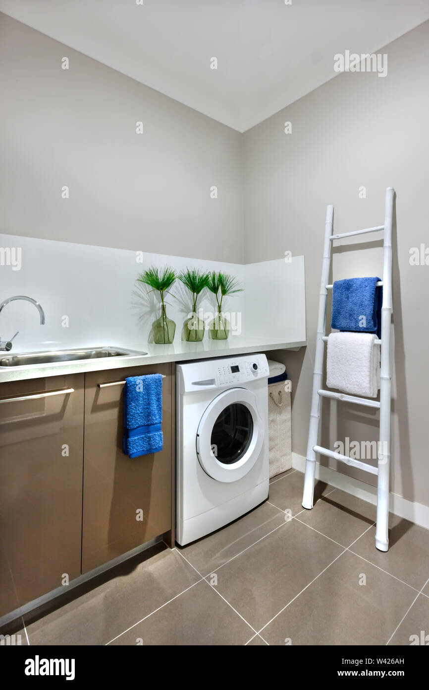Moderne, weiße Farbe Waschmaschine unter der Arbeitsplatte mit einem Hahn  und einem silbernen Waschbecken, die Waschmaschine ist mit weißen Fliesen  und der Wand ist eine graue Farbe. Th Stockfotografie - Alamy