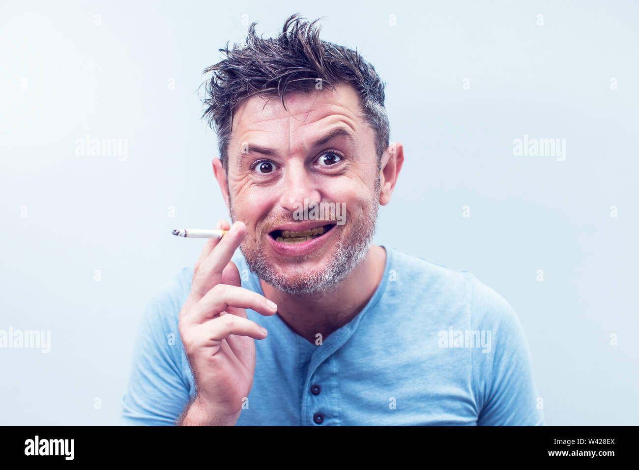 Hübscher junger Mann mit dem braunen Haar tragen Shirt auf grauem Hintergrund. Rauchen Zigarette. balack Zahn Stockfoto