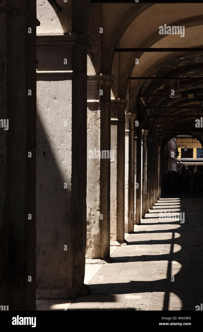 Porträtansicht von Säulen und Bögen mit Schatten rund um einen kleinen Platz, Venedig, Italien Stockfoto