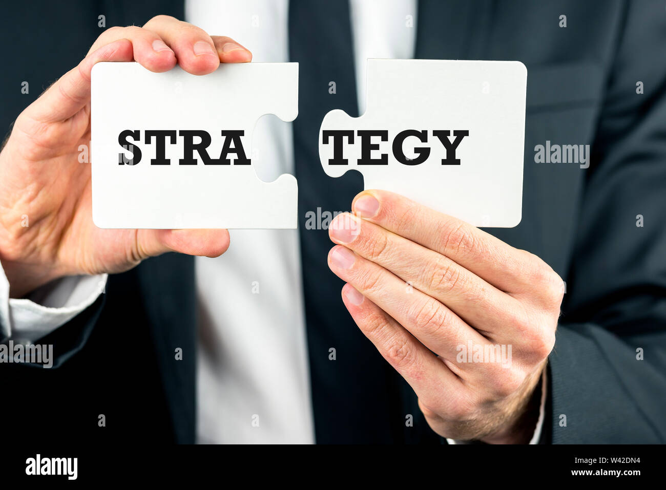 Nahaufnahme der Hände eines Geschäftsmannes, die zwei Teile eines Puzzles mit dem Wort Strategie über Sie Split konzeptionelle für zukunftsorientierte, plannin Stockfoto
