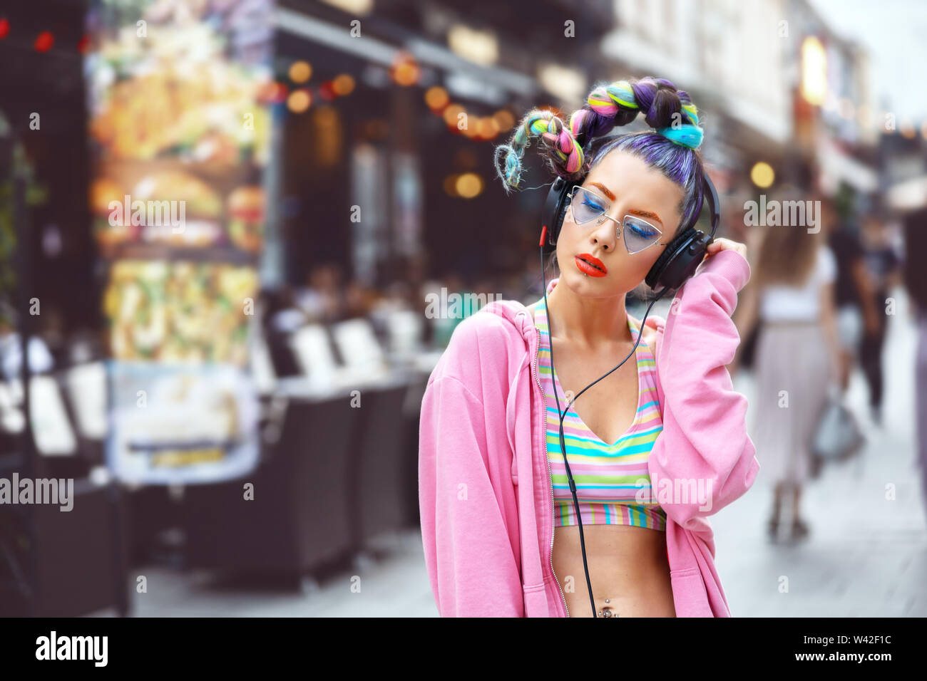 Cool funky junge Frau mit trendigen Avantgarde Musik hören über Kopfhörer im Freien Stockfoto