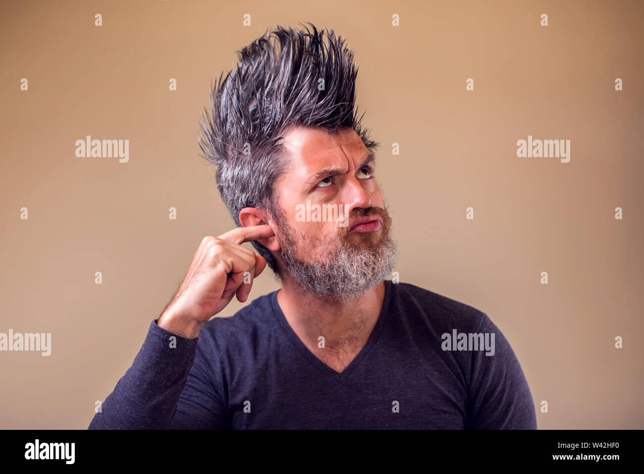 Mann mit Bart und Irokesen mit Finger im Ohr. Menschen und Emotionen Konzept Stockfoto