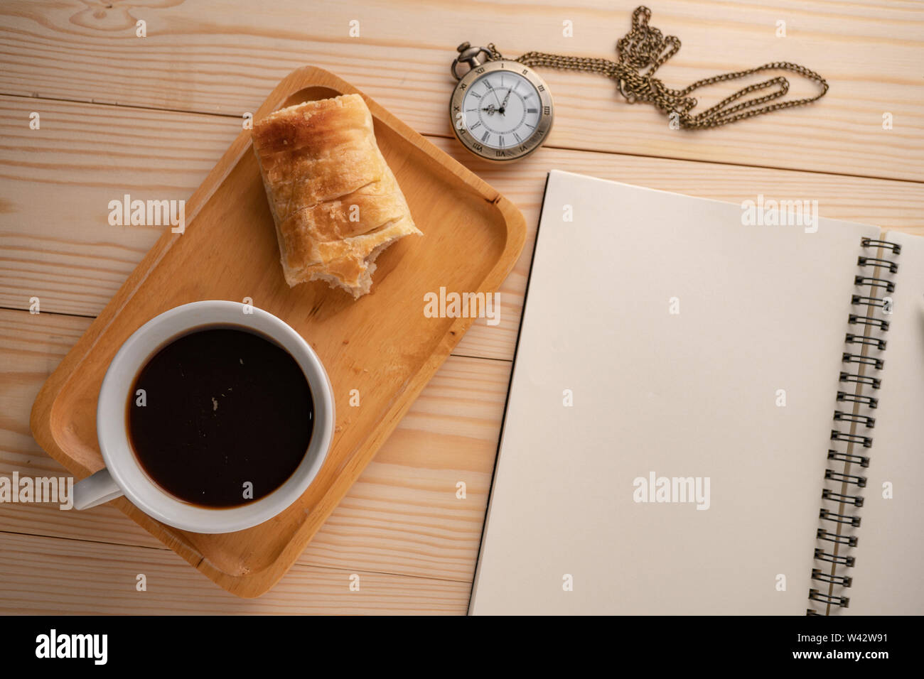 Blick von oben auf die Antique Gold Taschenuhr auf der Seite der Holz- Fach gelegt mit einem weißen Kaffeebecher und die Torte, gebissen worden und Leere noteboo Stockfoto