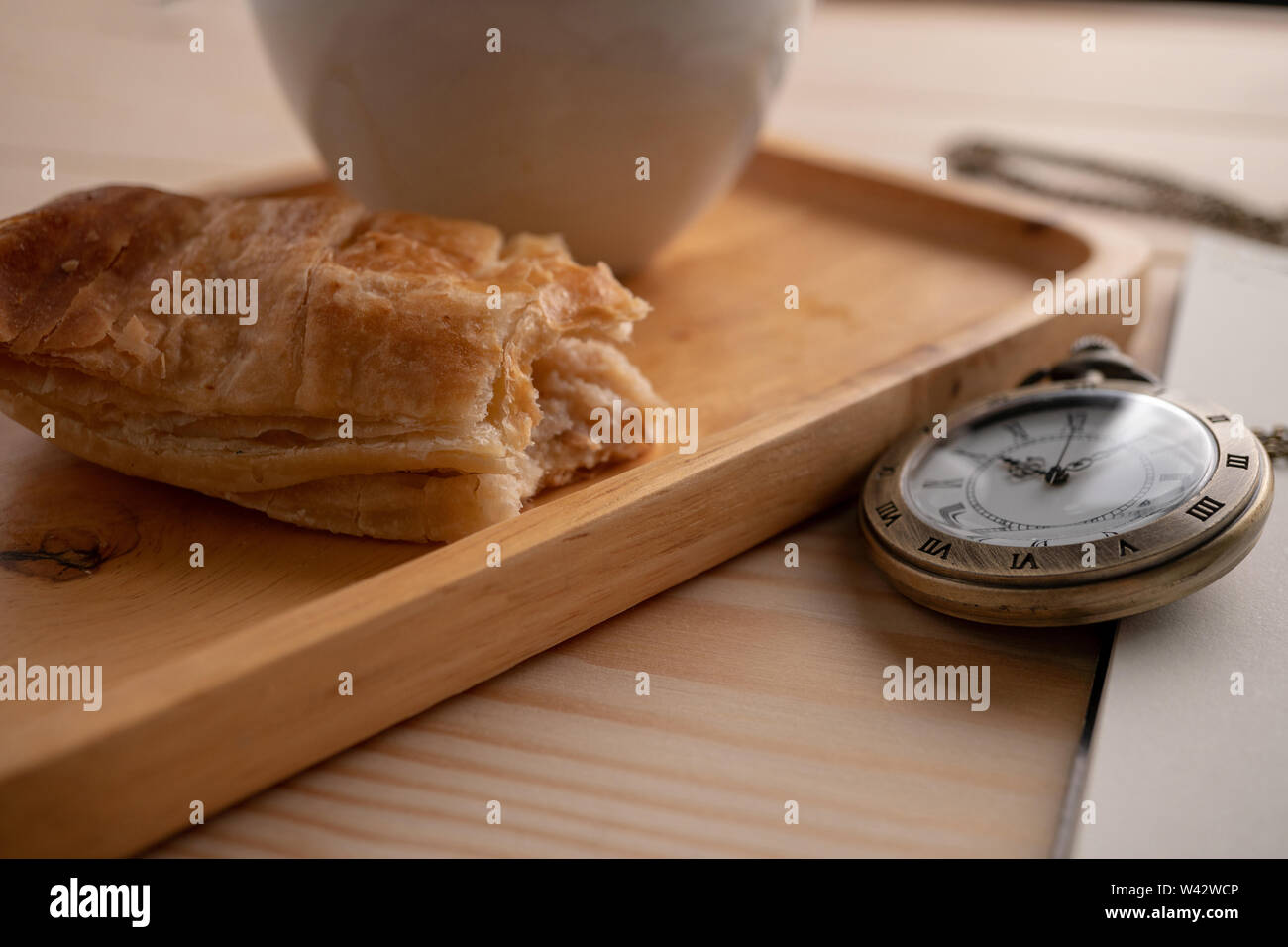 Antique Gold Taschenuhr auf der Seite der Holz- Fach gelegt mit einem weißen Kaffeebecher und die Torte, die gebissen wurde. Stockfoto