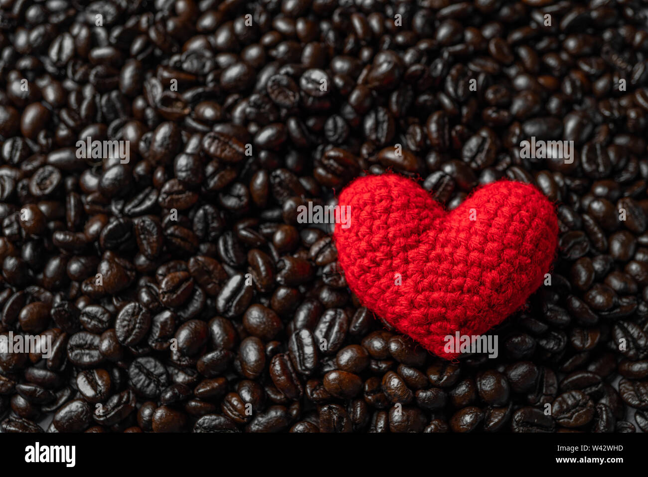 Rotes Herz auf eine Menge von gerösteten Kaffeebohnen Hintergrund. Starken schwarzen Kaffee Espresso, Körner, Hintergrund, Textur Stockfoto