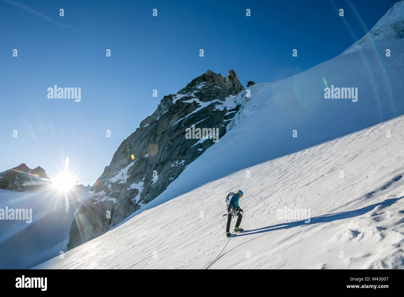 Ein Bergsteiger beginnt auf einem steilen Schneehang Wappen wie die Sonne den Horizont Stockfoto