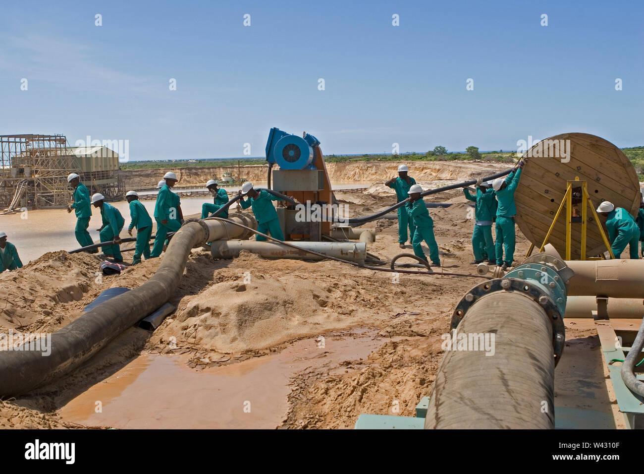 Bergbau, Verwaltung und Transport von Titanmineralsanden. Instandhaltungsteam verlegt neue Stromkabel an der Seite des Bergbauteichs für die Nassanlage dahinter. Stockfoto