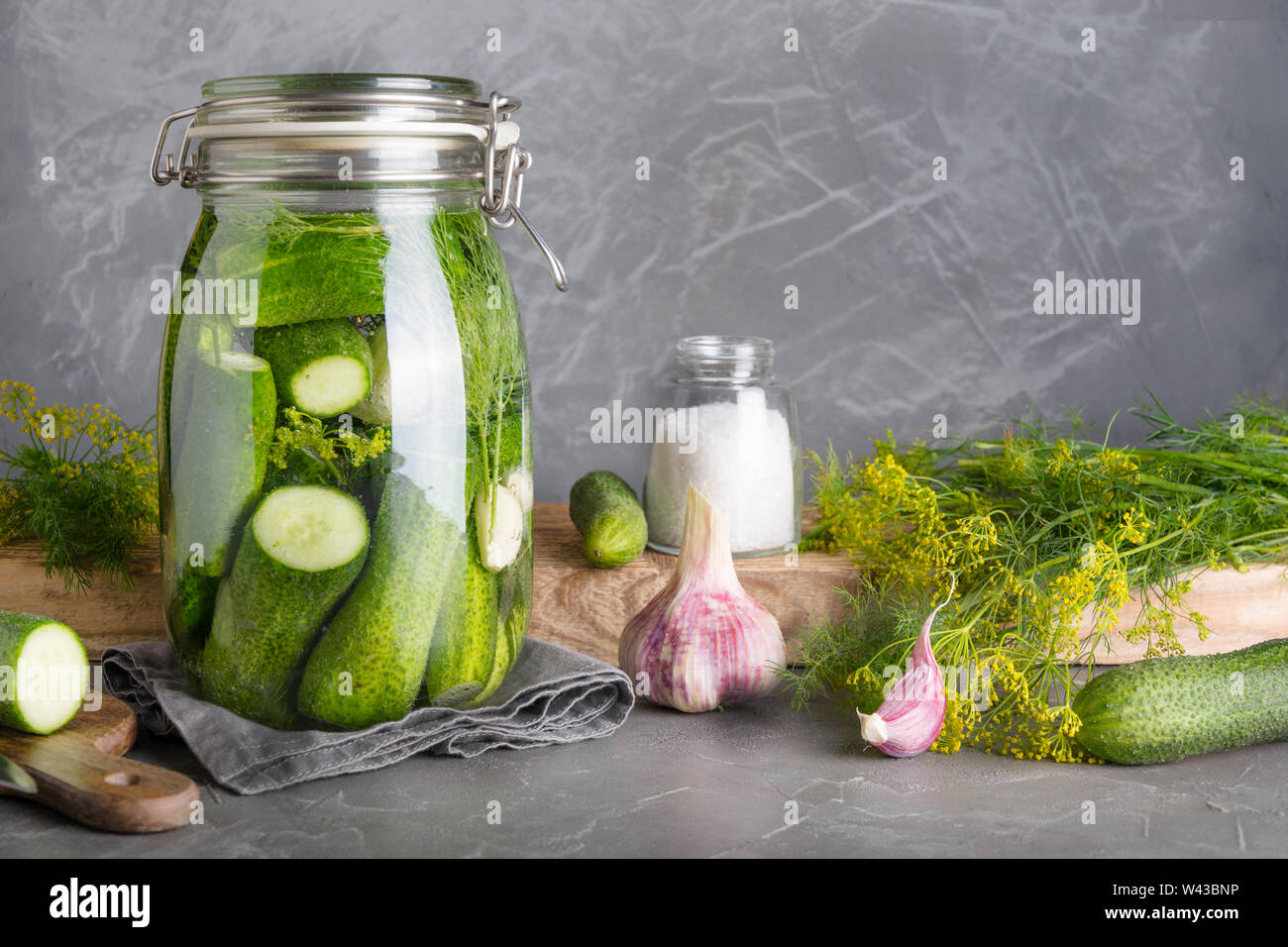 Beizen und Gärung Gurke in Glas Glas mit Dill und Knoblauch auf dunklem grauem Beton Tischplatte. Platz für Text und Design. Stockfoto