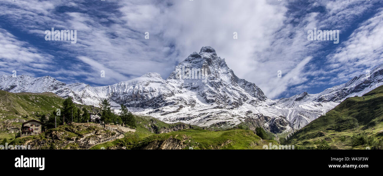 Panoramablick auf die Südseite des Matterhorns, Ansicht von Breuil-Cervinia Dorf. Grüne Wiese, die in der Front und blauer Himmel mit weißen Wolken Abo Stockfoto