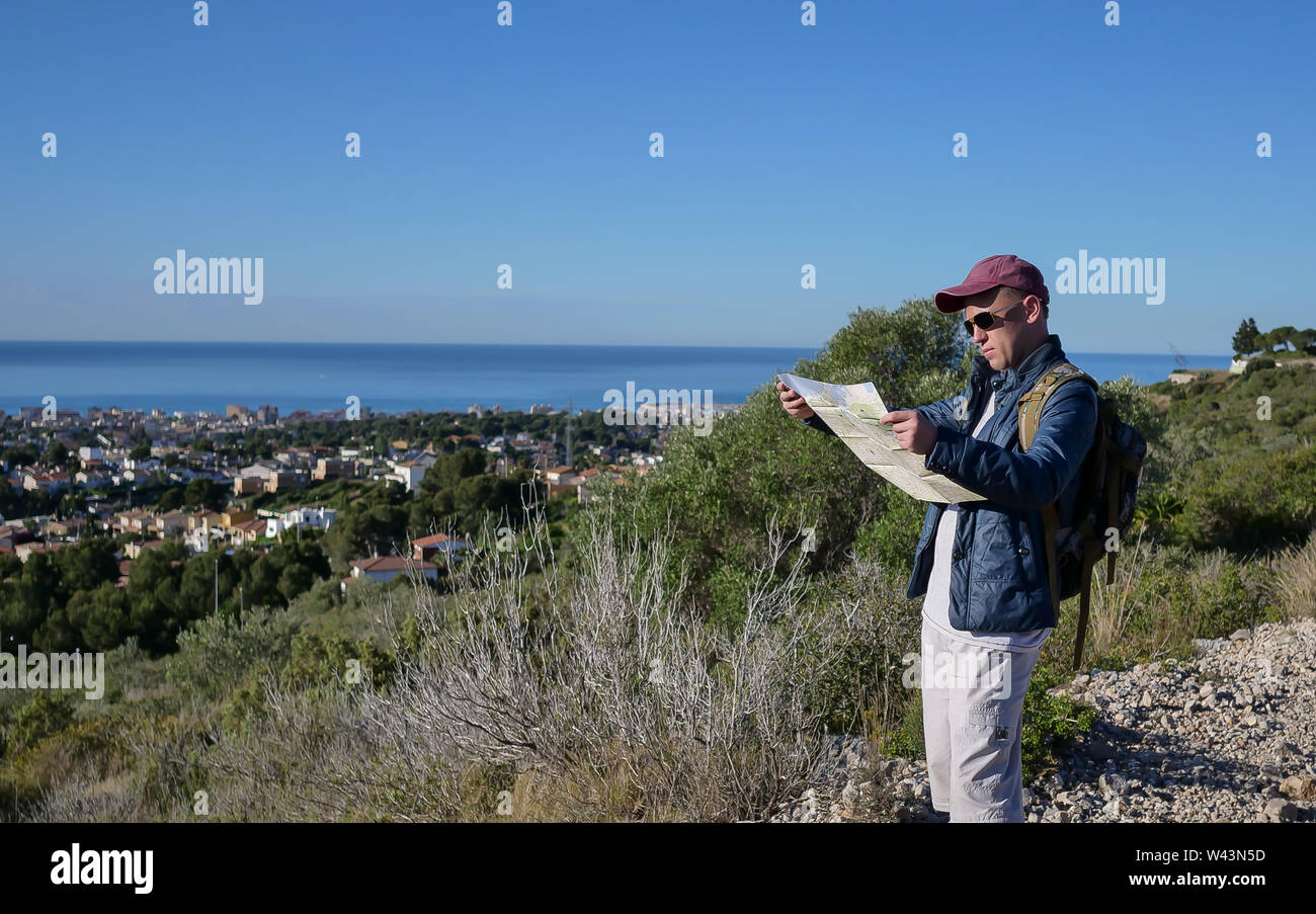 Der reisende Kerl steht auf einem Hügel und blickt auf eine Karte der Gegend Stockfoto