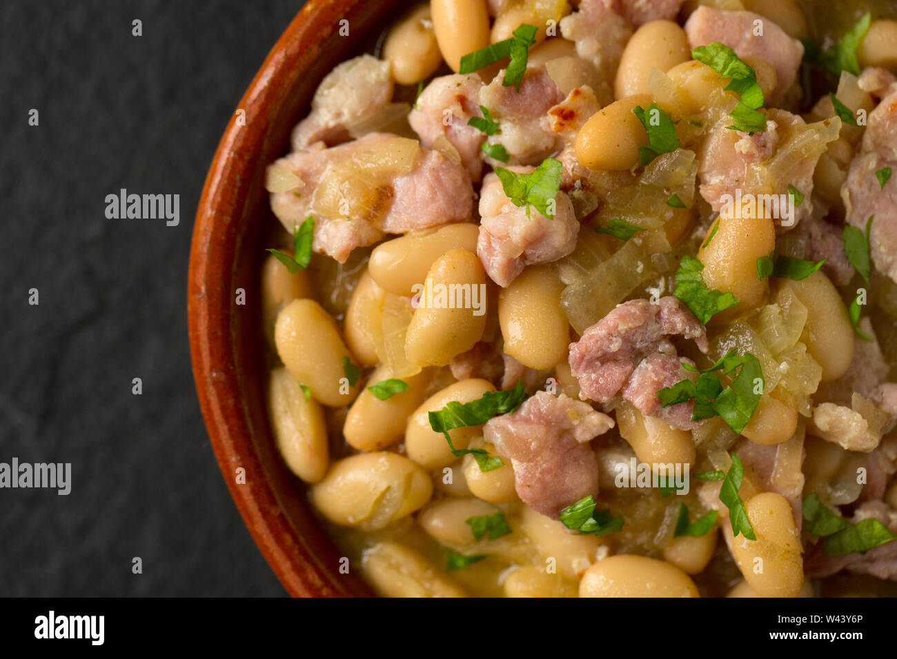 Eine Schüssel mit gebratenen Zwiebeln, Speck und verzinnten Cannellini-bohnen in Gemüsebrühe. Eine einfache und preiswerte Mahlzeit zu machen. Dorset England UK GB Stockfoto