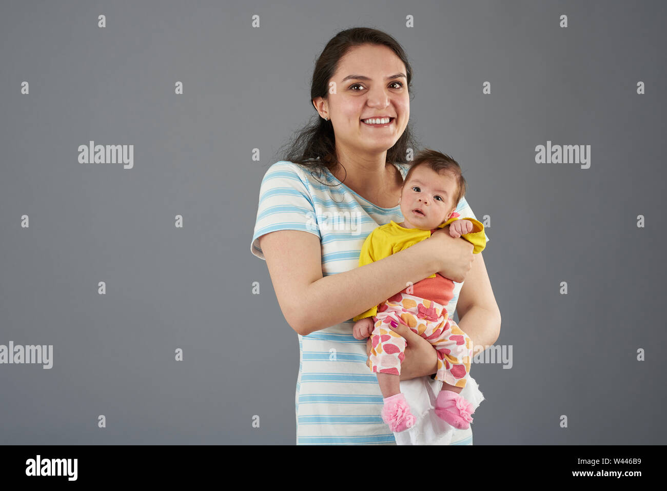 Glücklich lächelnde junge Mutter mit Baby Kind auf grauem Hintergrund Stockfoto