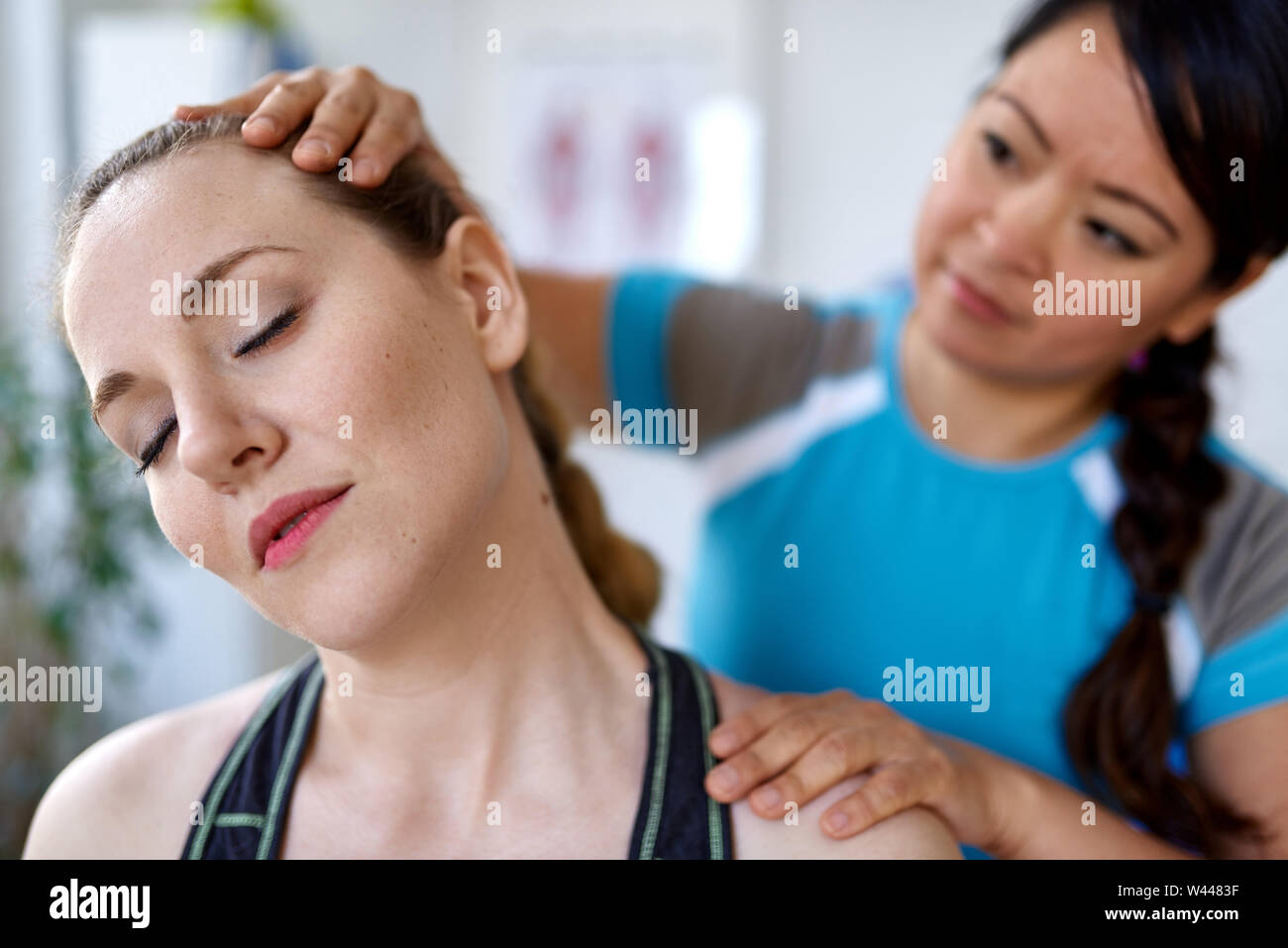 Chinesische Frau Physiotherapie Professional, eine Behandlung zu einer attraktiven Blondine Client in einem hellen Medizinisches Büro Stockfoto