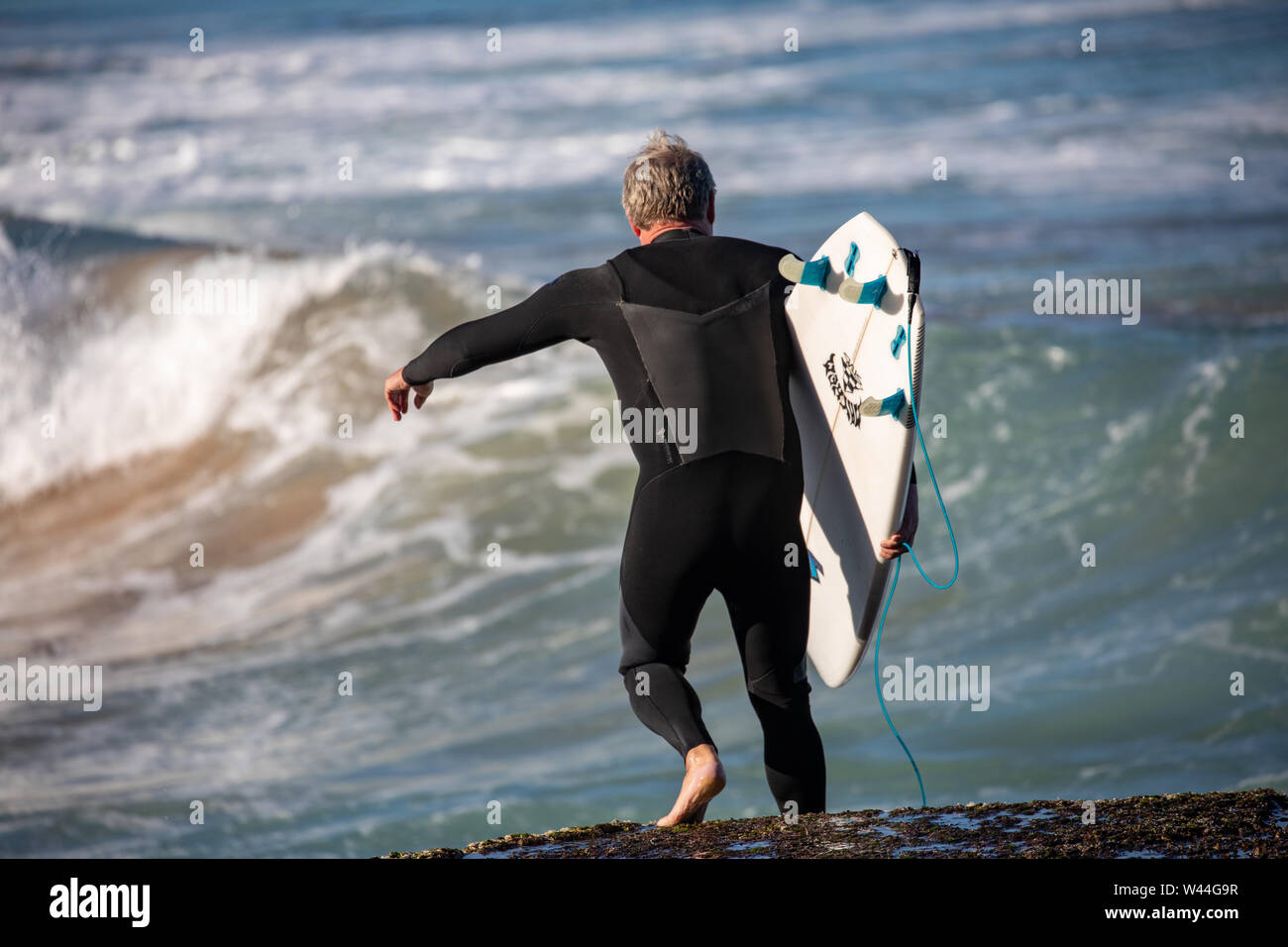 Australischer Mann trägt sein Surfbrett zum Ozean für ein Surfen auf den Wellen des Ozeans, Avalon Beach, Sydney, Australien Stockfoto