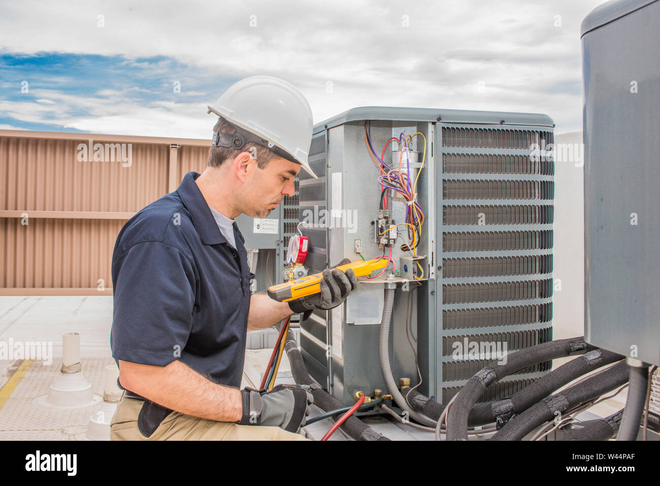 Hlk-Techniker mit einem Voltmeter ausgebildet, die Durchführung von vorbeugenden Wartungsarbeiten an einem Kondensator der Klimaanlage. Stockfoto